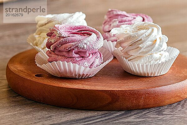 Rosa und weiße Marshmallows auf einem runden Holzbrett vor einem grauen Holzhintergrund. selektiver Fokus