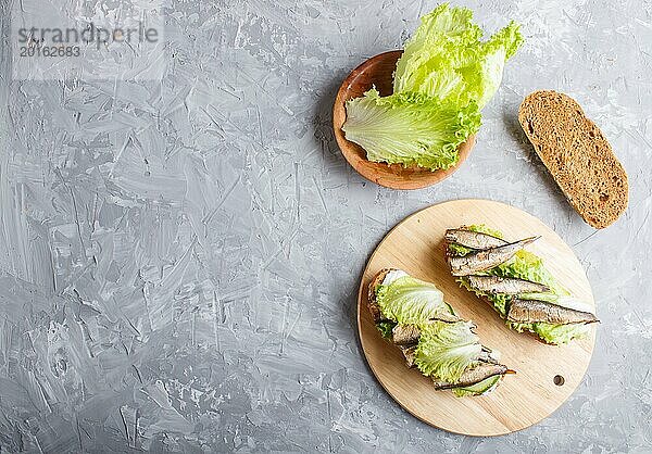 Sprotten Sandwiches mit Salat und Frischkäse auf Holzbrett auf grauem Betonhintergrund. Ansicht von oben  Kopierraum  Flat Lay