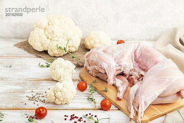 Ganzes rohes Kaninchen mit Blumenkohl  Tomaten und Gewürzen auf einem weißen Holzhintergrund und Leinenstoff. Seitenansicht  Nahaufnahme  selektiver Fokus