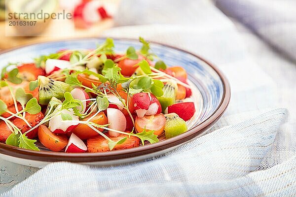 Vegetarischer Obst und Gemüsesalat aus Erdbeeren  Kiwi  Tomaten  Mikrogrünsprossen auf weißem Betonhintergrund und Leinentextil. Seitenansicht  Nahaufnahme  selektiver Fokus