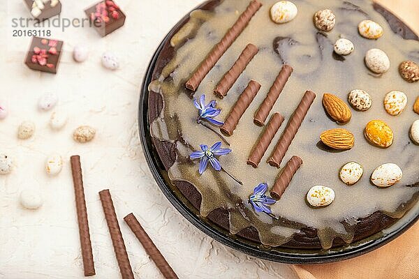 Hausgemachter Schokoladen Brownie Kuchen mit Karamellcreme und Mandeln mit einer Tasse Kaffee auf einem weißen Betonhintergrund und orangefarbenem Textil. Seitenansicht  Nahaufnahme  selektiver Fokus