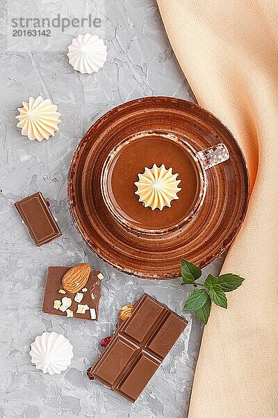 Tasse heiße Schokolade und Stücke von Milchschokolade mit Mandeln auf einem grauen Betonhintergrund mit orangefarbenem Textil. Draufsicht  Flachlegung  Nahaufnahme