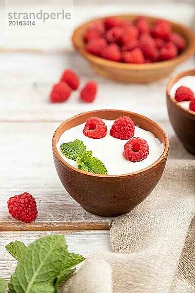 Joghurt mit Himbeeren in Tonbechern auf weißem Holzhintergrund und Leinentuch. Seitenansicht  Nahaufnahme  selektiver Fokus