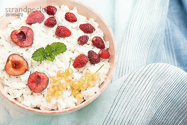 Reisflockenbrei mit Milch und Erdbeere in Keramikschüssel auf weißem Betonhintergrund und blauem Leinentextil. Draufsicht  flach gelegt  Nahaufnahme