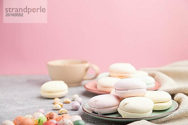 Bunte Zephir oder Marshmallow mit Tasse Kaffee und Dragees auf einem grauen und rosa Hintergrund und Leinenstoff. Seitenansicht  Nahaufnahme  selektiver Fokus  Kopierraum