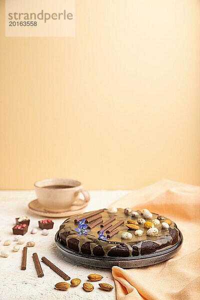 Hausgemachter Schokoladen Brownie Kuchen mit Karamellcreme und Mandeln mit einer Tasse Kaffee auf einem weißen und orangefarbenen Hintergrund und orangefarbenem Textil. Seitenansicht  Kopierraum  selektiver Fokus