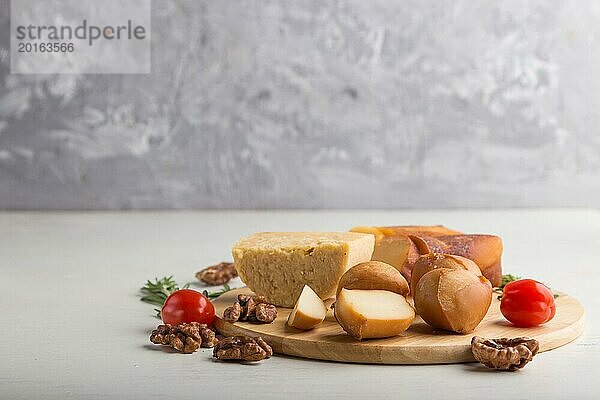 Geräucherter Käse und verschiedene Käsesorten mit Rosmarin und Tomaten auf einem Holzbrett auf einem grauen und weißen Hintergrund. Seitenansicht  Kopierraum  selektiver Fokus