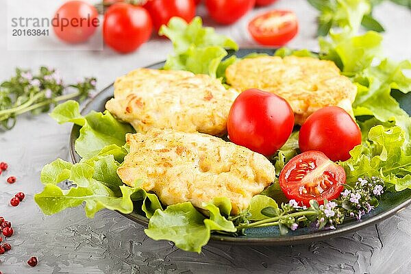 Gehackte Hähnchenschnitzel mit Salat  Tomaten und Kräutern auf einem grauen Betonhintergrund. Seitenansicht  Nahaufnahme  selektiver Fokus