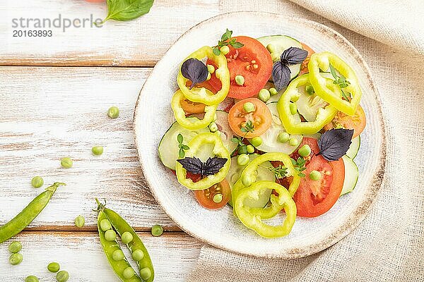 Vegetarischer Salat aus grünen Erbsen  Tomaten  Paprika und Basilikum auf weißem Holzhintergrund und Leinentextil. Draufsicht  Nahaufnahme  Flat Lay  selektiver Fokus