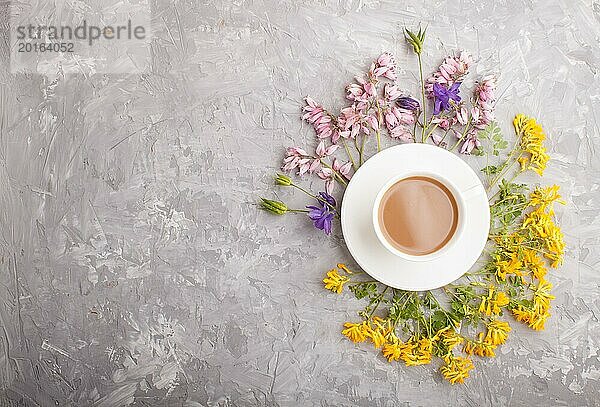 Gelbe  rosa und blaue Blumen in einer Spirale und eine Tasse Kaffee auf einem grauen Hintergrund aus Beton. Morninig  Frühling  Mode Zusammensetzung. Flachlage  Draufsicht  Kopierraum