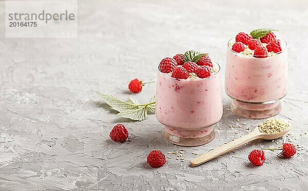 Joghurt mit Himbeere und Sesam in einem Glas und Holzlöffel auf grauem Betonhintergrund. Seitenansicht  Kopierraum  selektiver Fokus