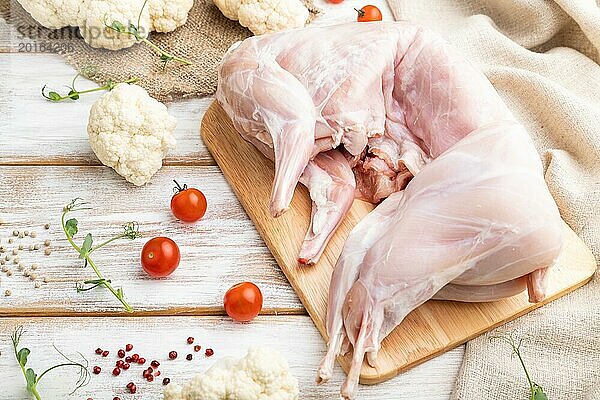 Ganzes rohes Kaninchen mit Blumenkohl  Tomaten und Gewürzen auf einem weißen Holzhintergrund und Leinenstoff. Seitenansicht  Nahaufnahme  selektiver Fokus