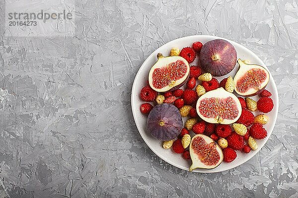 Frische Feigen  Erdbeeren und Himbeeren auf weißem Keramikteller auf grauem Betonhintergrund. Draufsicht  flat lay  copy space