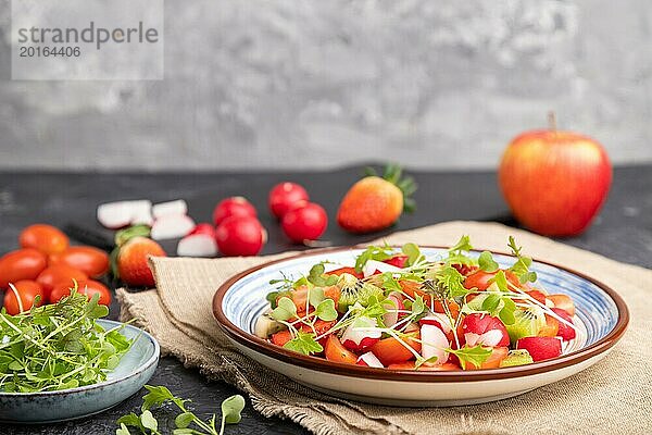 Vegetarischer Obst und Gemüsesalat aus Erdbeeren  Kiwi  Tomaten  Mikrogrünsprossen auf schwarzem und grauem Hintergrund und Leinentuch. Seitenansicht  selektiver Fokus  Kopierraum