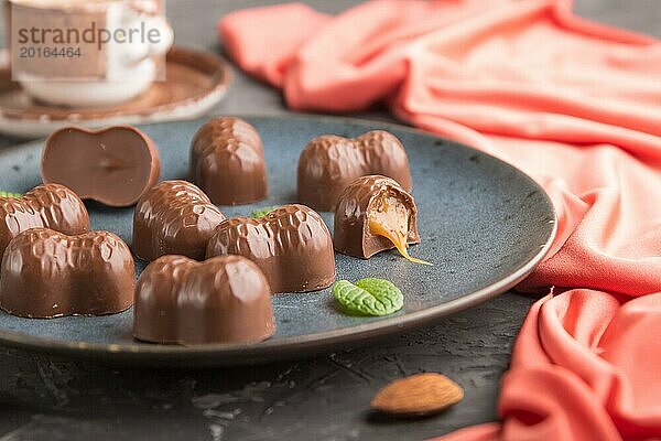 Schokoladenkaramellbonbons mit Mandeln und einer Tasse Kaffee auf einem schwarzen Betonhintergrund und rotem Textil. Seitenansicht  Nahaufnahme  selektiver Fokus