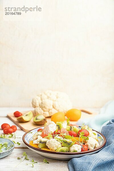 Vegetarischer Salat aus Blumenkohl  Kiwi  Tomaten  Mikrogrünsprossen auf weißem Holzhintergrund und blauem Leinentuch. Seitenansicht  Kopierraum  selektiver Fokus