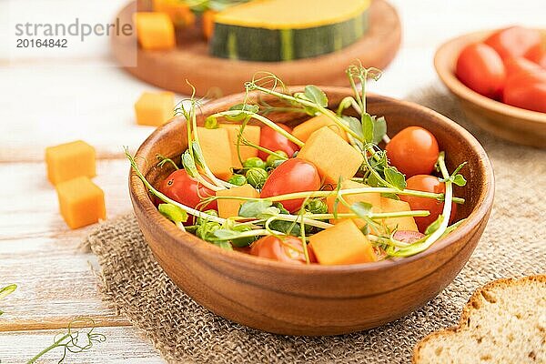 Vegetarischer Gemüsesalat aus Tomaten  Kürbis  mikrogrünen Erbsensprossen auf weißem Holzhintergrund und Leinentuch. Seitenansicht  Nahaufnahme  selektiver Fokus