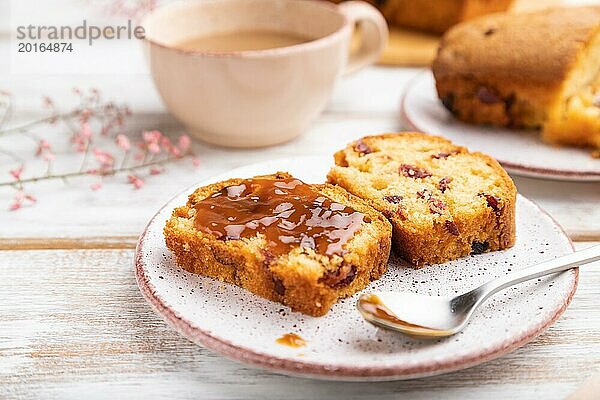 Hausgemachter Kuchen mit Rosinen  Mandeln  weichem Karamell und einer Tasse Kaffee auf einem weißen Holzhintergrund. Seitenansicht  Nahaufnahme  selektiver Fokus