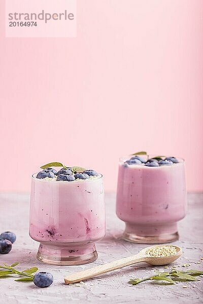 Joghurt mit Heidelbeeren und Sesam in einem Glas und Holzlöffel auf grauem und rosa Hintergrund. Seitenansicht  Nahaufnahme