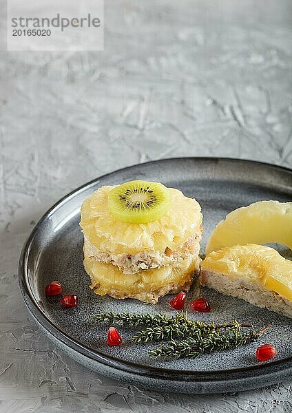 Stücke von gebackenem Schweinefleisch mit Ananas  Käse und Kiwi auf grauem Teller  Seitenansicht  Nahaufnahme  selektiver Fokus  Kopierraum