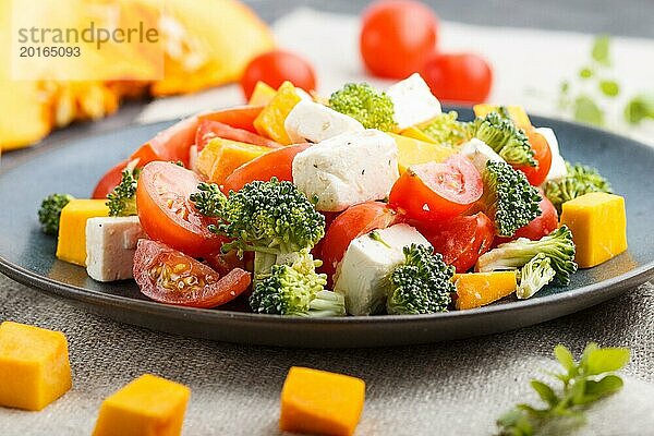 Vegetarischer Salat mit Brokkoli  Tomaten  Fetakäse und Kürbis auf einem blauen Keramikteller auf schwarzem Betonhintergrund und Leinentuch  Seitenansicht  Nahaufnahme  selektiver Fokus