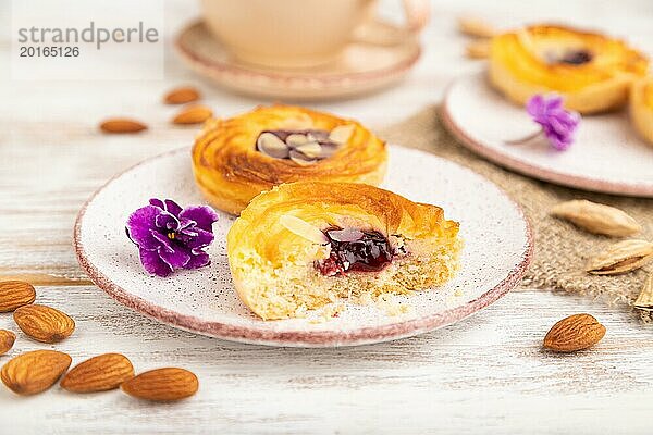 Kleine Käsekuchen mit Marmelade und Mandeln mit einer Tasse Kaffee auf einem weißen Holzhintergrund und Leinenstoff. Seitenansicht  Nahaufnahme  selektiver Fokus