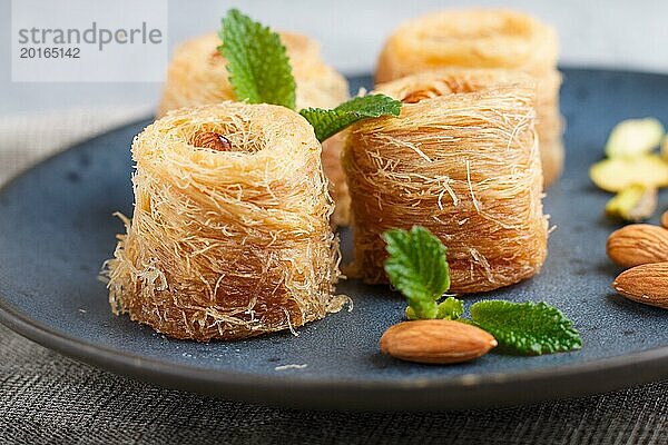 Kunafa  traditionelle arabische Süßigkeiten in blauem Keramikteller auf grauem Betonhintergrund. Seitenansicht  Nahaufnahme  selektiver Fokus