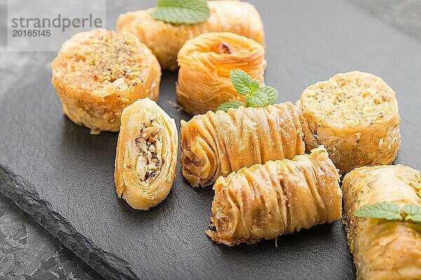 Traditionelle arabische Süßigkeiten (kunafa  baklava) auf einer schwarzen Schiefertafel auf einem schwarzen Betonhintergrund. Seitenansicht  Nahaufnahme  selektiver Fokus