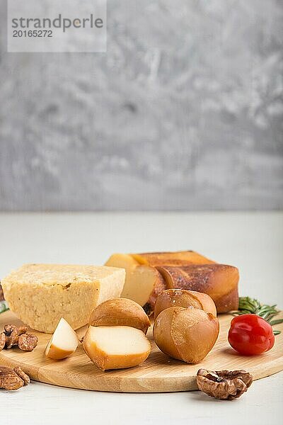 Geräucherter Käse und verschiedene Käsesorten mit Rosmarin und Tomaten auf einem Holzbrett auf einem grauen und weißen Hintergrund. Seitenansicht  Kopierraum  selektiver Fokus