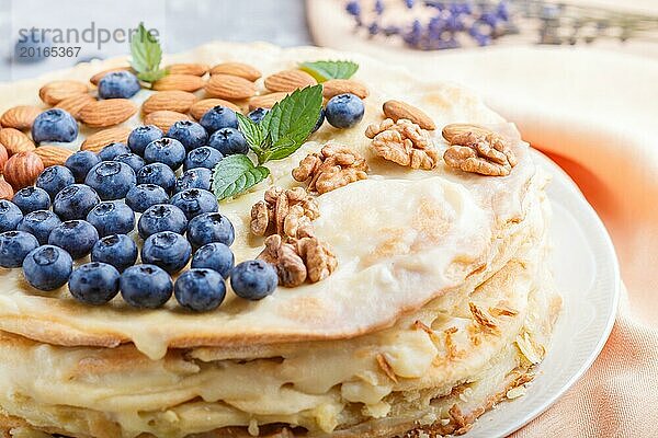 Hausgemachte geschichtete Napoleon Torte mit Milchcreme. Dekoriert mit Blaubeere  Mandeln  Walnüsse  Haselnüsse  Minze auf einem grauen Beton Hintergrund. Seitenansicht  selektiver Fokus  Nahaufnahme