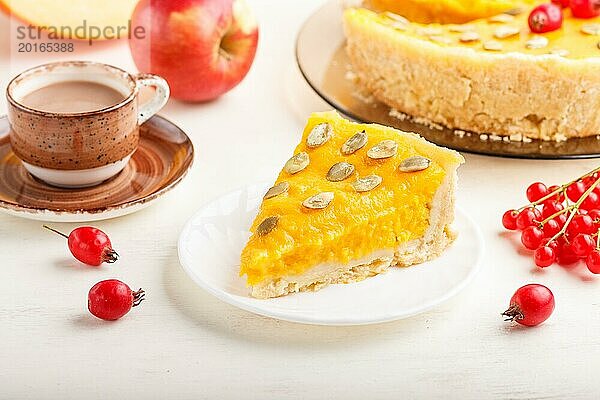 Traditioneller amerikanischer süßer Kürbiskuchen  verziert mit roten Weißdornbeeren und Kürbiskernen  mit einer Tasse Kaffee auf einem weißen Holzhintergrund. Seitenansicht  Nahaufnahme  selektiver Fokus