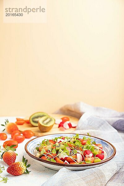 Vegetarischer Obst und Gemüsesalat mit Erdbeeren  Kiwi  Tomaten  mikrogrünen Sprossen auf weißem und orangefarbenem Hintergrund und Leinentuch. Seitenansicht  Kopierraum  selektiver Fokus