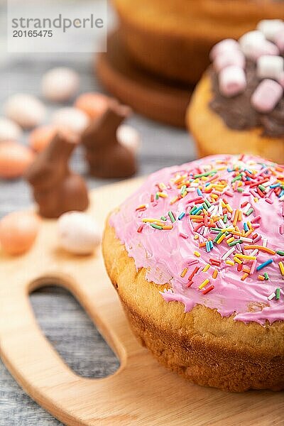 Hausgemachte glasierte und dekorierte Osterkuchen mit Schokoladeneiern und Kaninchen auf grauem Holzhintergrund und Leinentextil. Seitenansicht  selektiver Fokus  Nahaufnahme