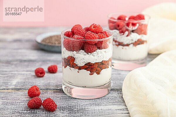 Joghurt mit Himbeeren  Goji Beeren und Chia Samen im Glas auf grauem Holzhintergrund und Leinenstoff. Seitenansicht  Nahaufnahme  selektiver Fokus