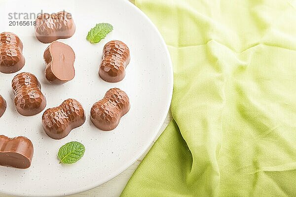 Schokoladenbonbons mit Mandeln auf einem weißen Holzhintergrund und grünem Textil. Seitenansicht  Nahaufnahme  selektiver Fokus