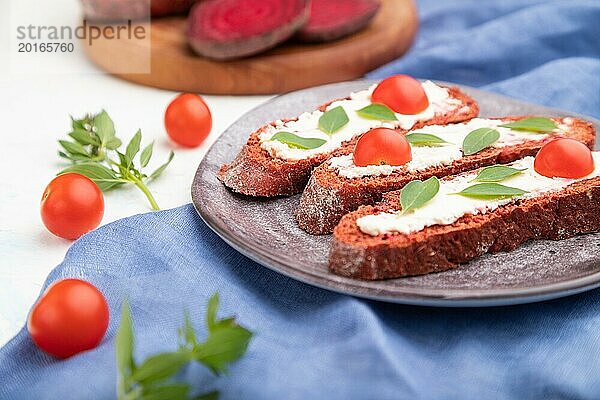 Rote Bete Brote mit Frischkäse und Tomaten auf weißem Betonhintergrund und blauem Leinentextil. Seitenansicht  selektiver Fokus  Nahaufnahme