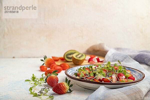 Vegetarischer Obst und Gemüsesalat aus Erdbeeren  Kiwi  Tomaten  Mikrogrünsprossen auf weißem Betonhintergrund und Leinentuch. Seitenansicht  Kopierraum  selektiver Fokus