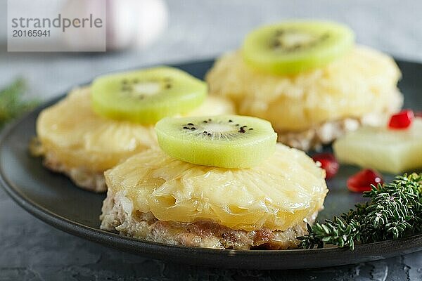 Stücke von gebackenem Schweinefleisch mit Ananas  Käse und Kiwi auf grauem Hintergrund  Seitenansicht  Nahaufnahme  selektiver Fokus