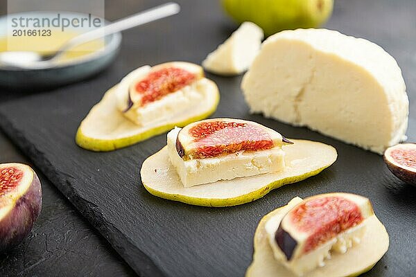 Sommerliche Vorspeise mit Birne  Hüttenkäse  Feigen und Honig auf Schieferplatte auf schwarzem Betonhintergrund. Seitenansicht  Nahaufnahme  selektiver Fokus