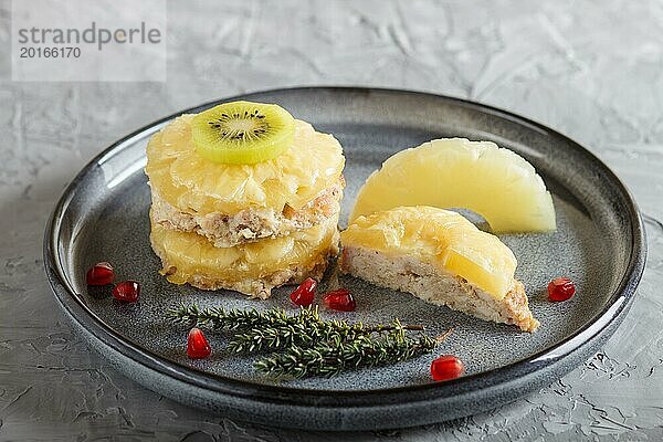 Stücke von gebackenem Schweinefleisch mit Ananas  Käse und Kiwi auf grauem Teller  Seitenansicht  Nahaufnahme  selektiver Fokus