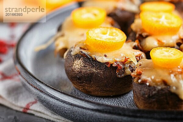 Gefüllte gebratene Champignons mit Käse  Kumquats und grünen Erbsen auf einem grauen Betonhintergrund. Keramikteller  Seitenansicht  Nahaufnahme  selektiver Fokus