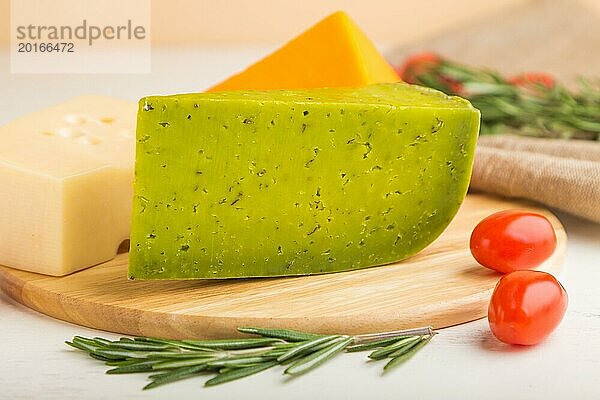 Grüner Basilikumkäse und verschiedene Käsesorten mit Rosmarin und Tomaten auf einem Holzbrett auf einem weißen Holzhintergrund. Seitenansicht  Nahaufnahme  selektiver Fokus