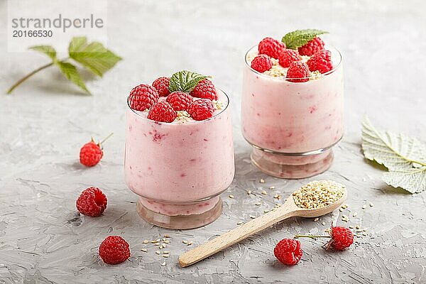 Joghurt mit Himbeere und Sesam in einem Glas und Holzlöffel auf grauem Betonhintergrund. Seitenansicht  Nahaufnahme