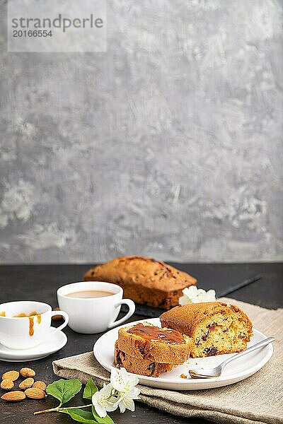 Hausgemachter Kuchen mit Rosinen  Mandeln  weichem Karamell und einer Tasse Kaffee auf schwarzem Betonhintergrund und Leinenstoff. Seitenansicht  Kopierraum  selektiver Fokus