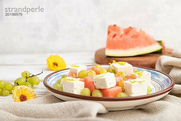 Vegetarischer Salat mit Wassermelone  Fetakäse und Trauben auf blauem Keramikteller auf weißem Holzhintergrund und Leinentuch. Seitenansicht  Nahaufnahme  selektiver Fokus