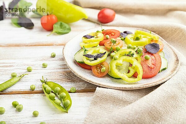 Vegetarischer Salat aus grünen Erbsen  Tomaten  Paprika und Basilikum auf weißem Holzhintergrund und Leinentuch. Seitenansicht  Nahaufnahme  selektiver Fokus