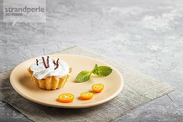 Kuchen mit Schlagsahne auf einem hellbraunen Teller mit Kumquatscheiben und Minzblättern auf grauem Betonhintergrund mit Leinenserviette. selektiver Fokus  Kopierraum  Seitenansicht