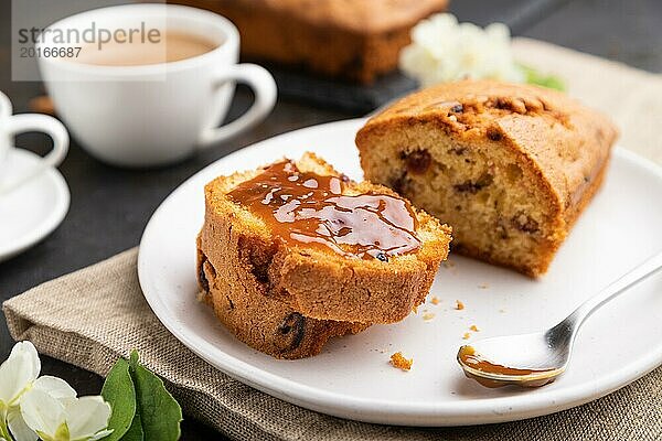 Hausgemachter Kuchen mit Rosinen  Mandeln  weichem Karamell und einer Tasse Kaffee auf einem schwarzen Betonhintergrund und Leinenstoff. Seitenansicht  Nahaufnahme  selektiver Fokus