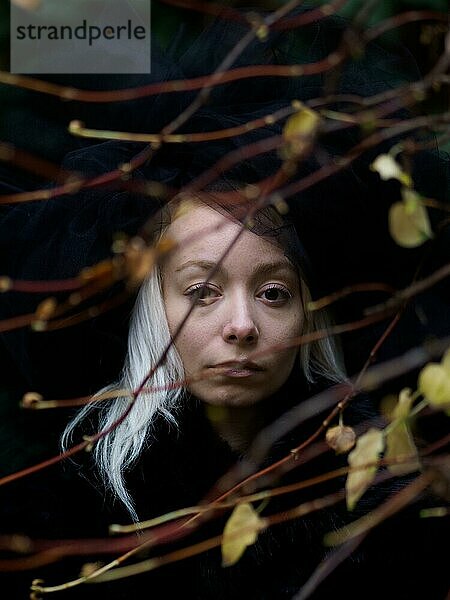Kaukasisches junges platinblondes Frauengesicht  das teilweise von Herbstblättern verdeckt wird  was eine rätselhafte  dunkle Gothic Stimmung erzeugt