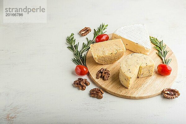 Cheddar und verschiedene Käsesorten mit Rosmarin und Tomaten auf einem Holzbrett vor einem weißen Holzhintergrund. Seitenansicht  Kopierraum  selektiver Fokus